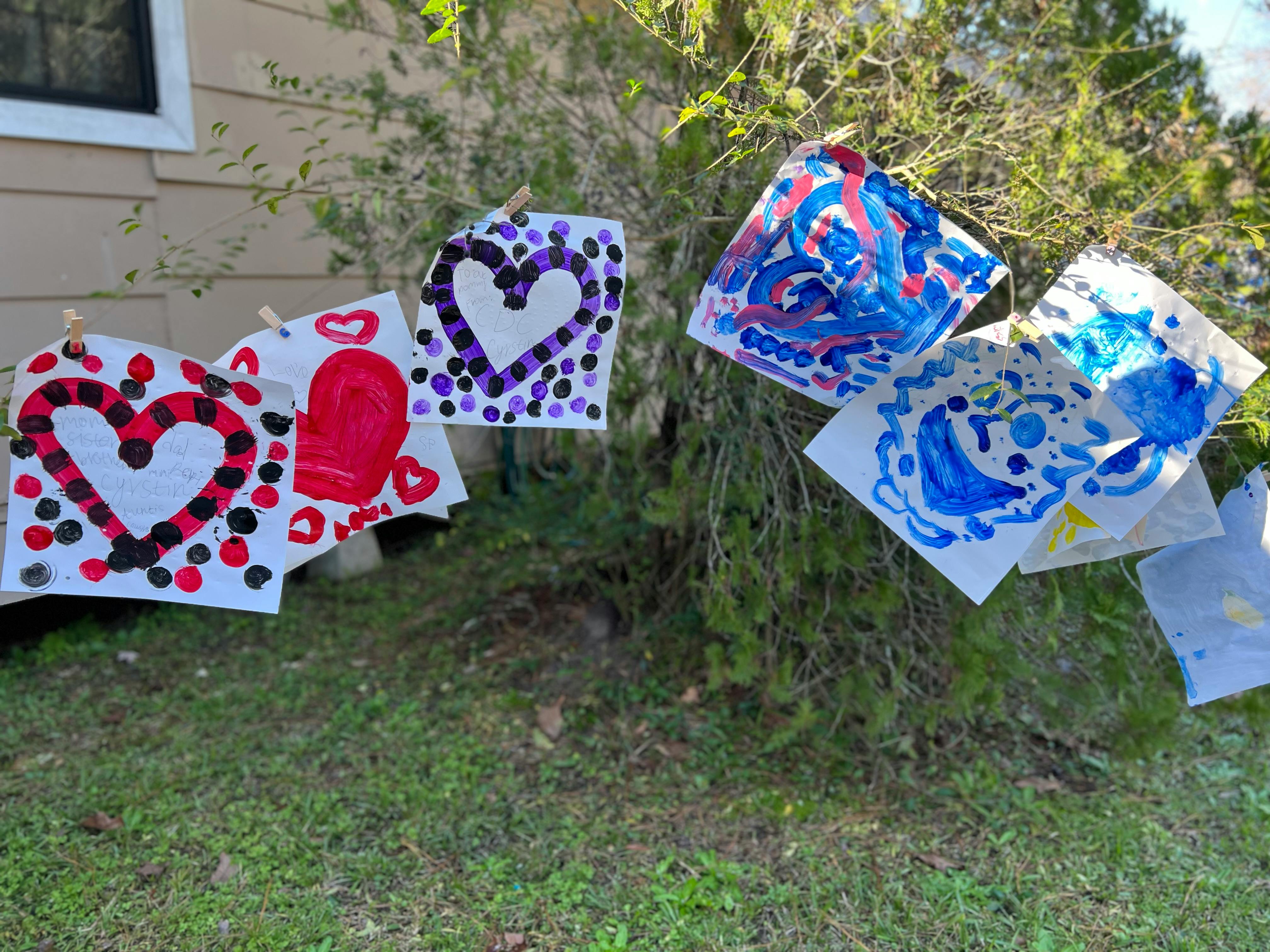 Children's artwork with hearts and abstract designs hanging on a bush