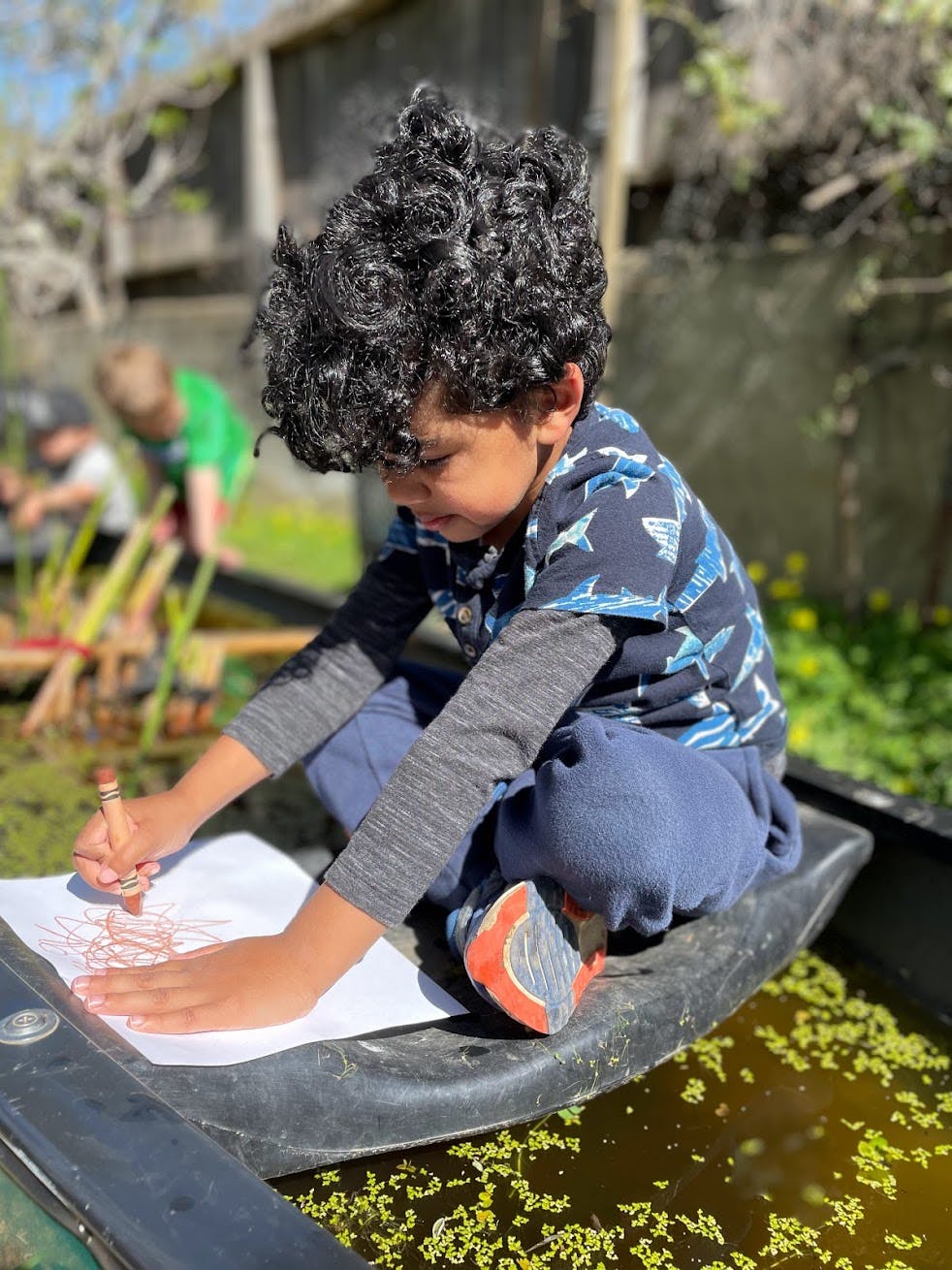 Child drawing on paper with a crayon outdoors