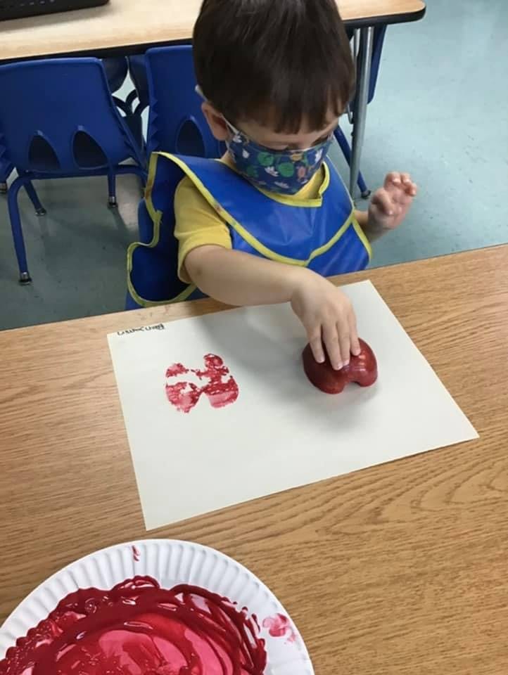 Child in mask and apron doing red heart print art