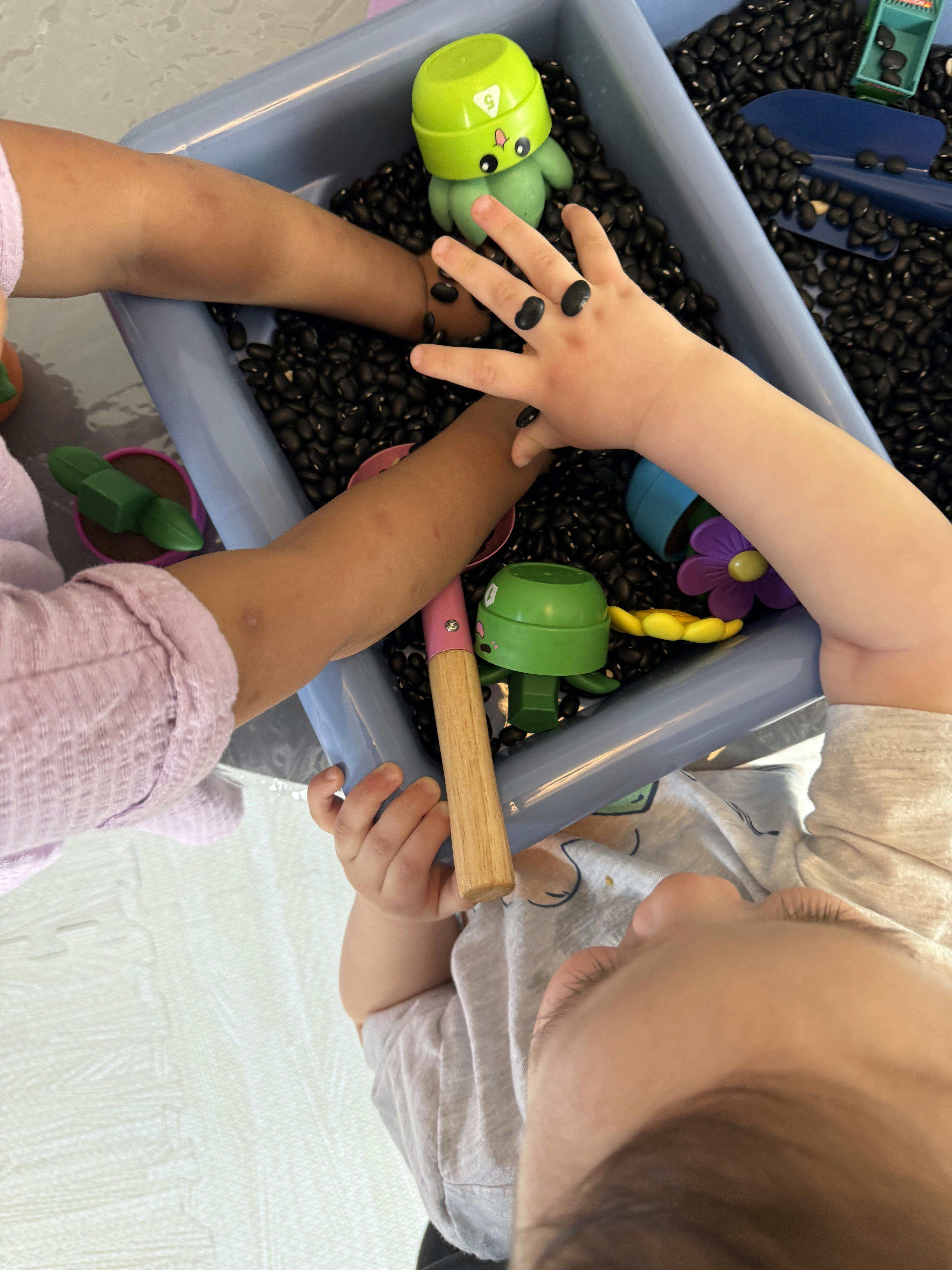 Children playing with toys in a bin filled with dried black beans