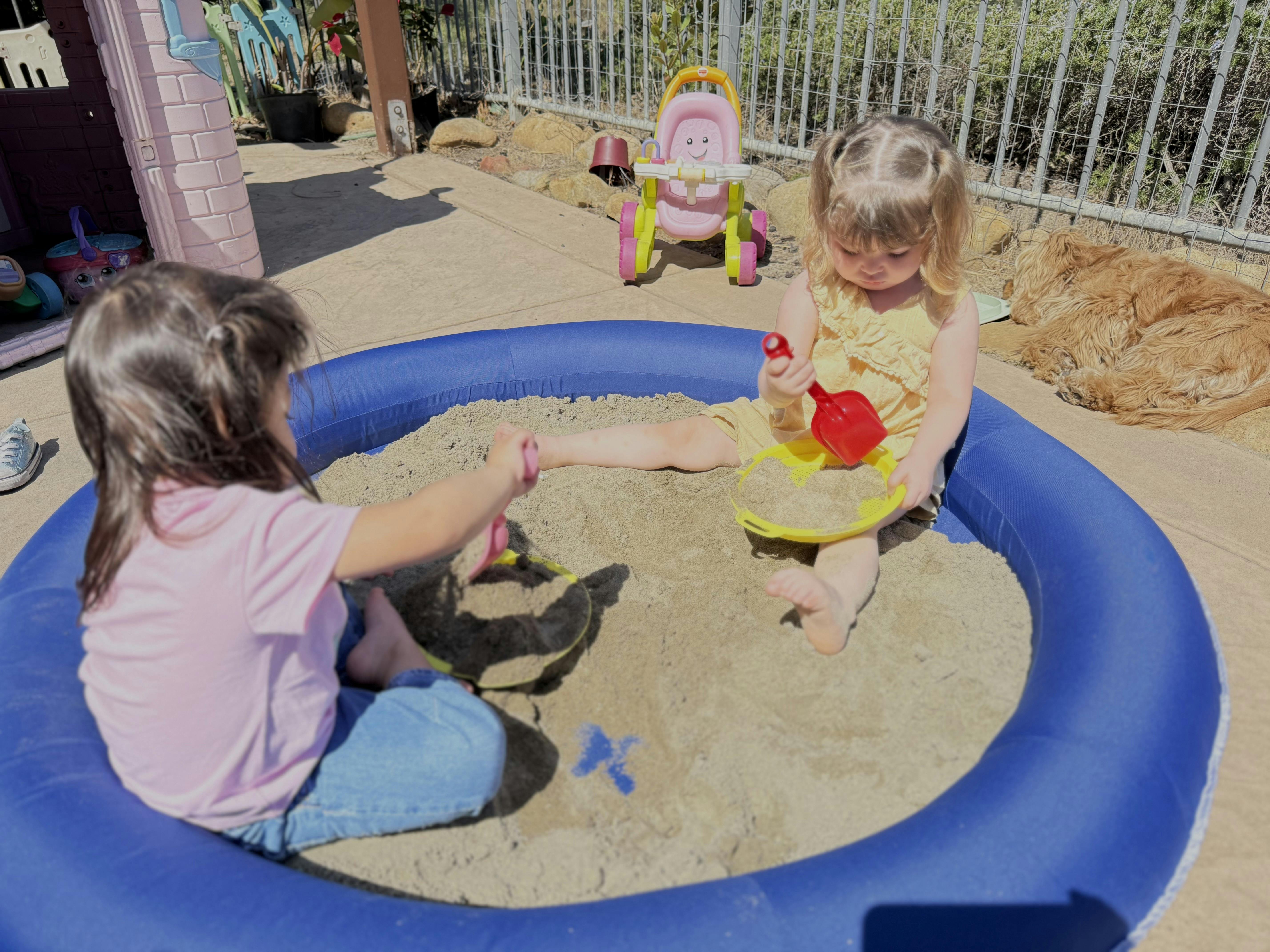 Two children playing in a blue sand pit with shovels and sifters
