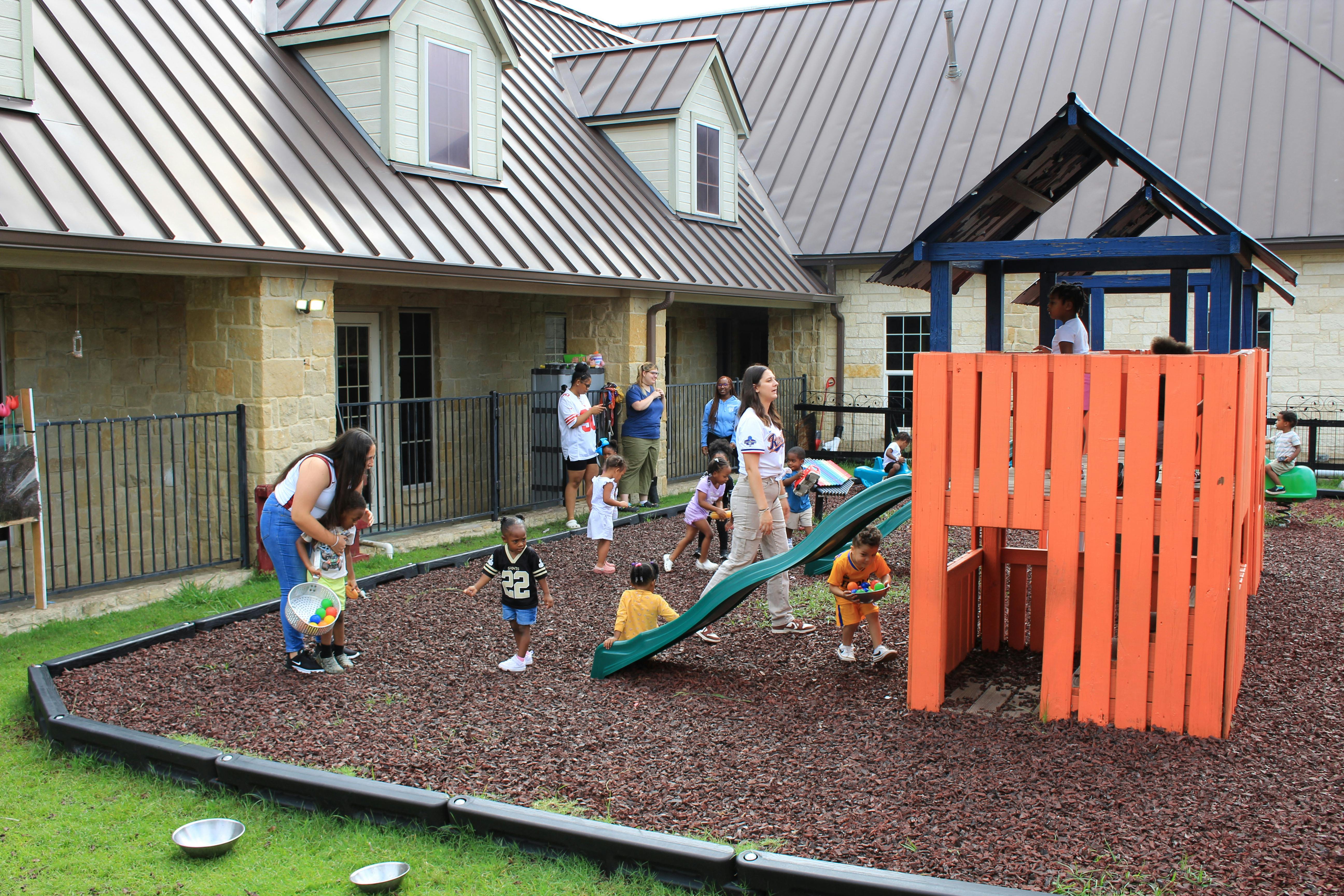 People and children on a playground with a slide and play structure