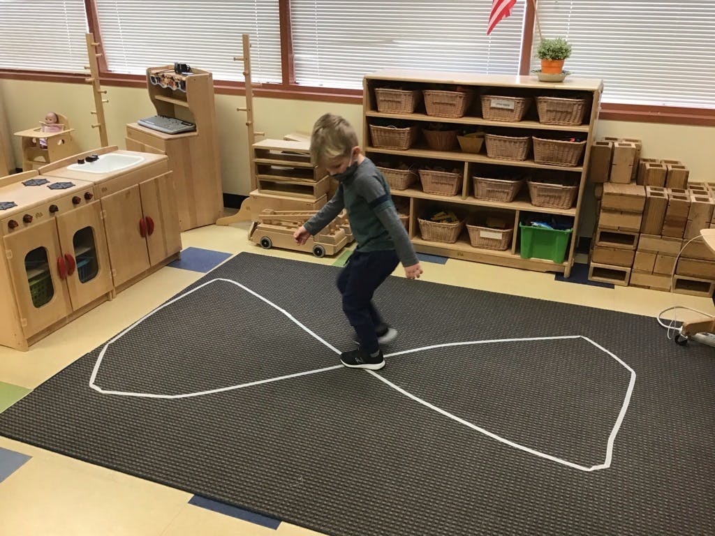 Child balancing on a figure-eight outline on a rug in a classroom