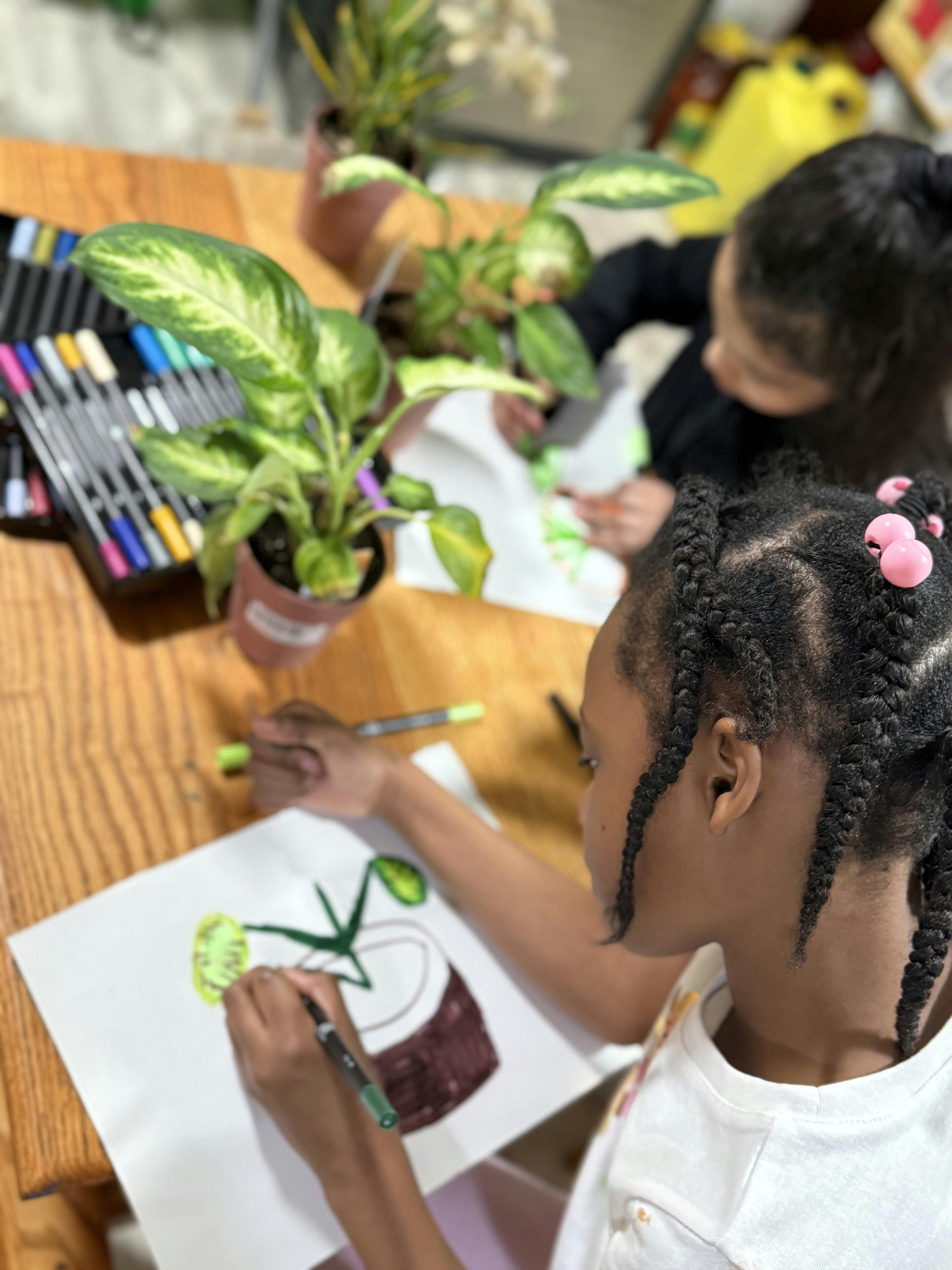Child drawing a plant in a pot with markers