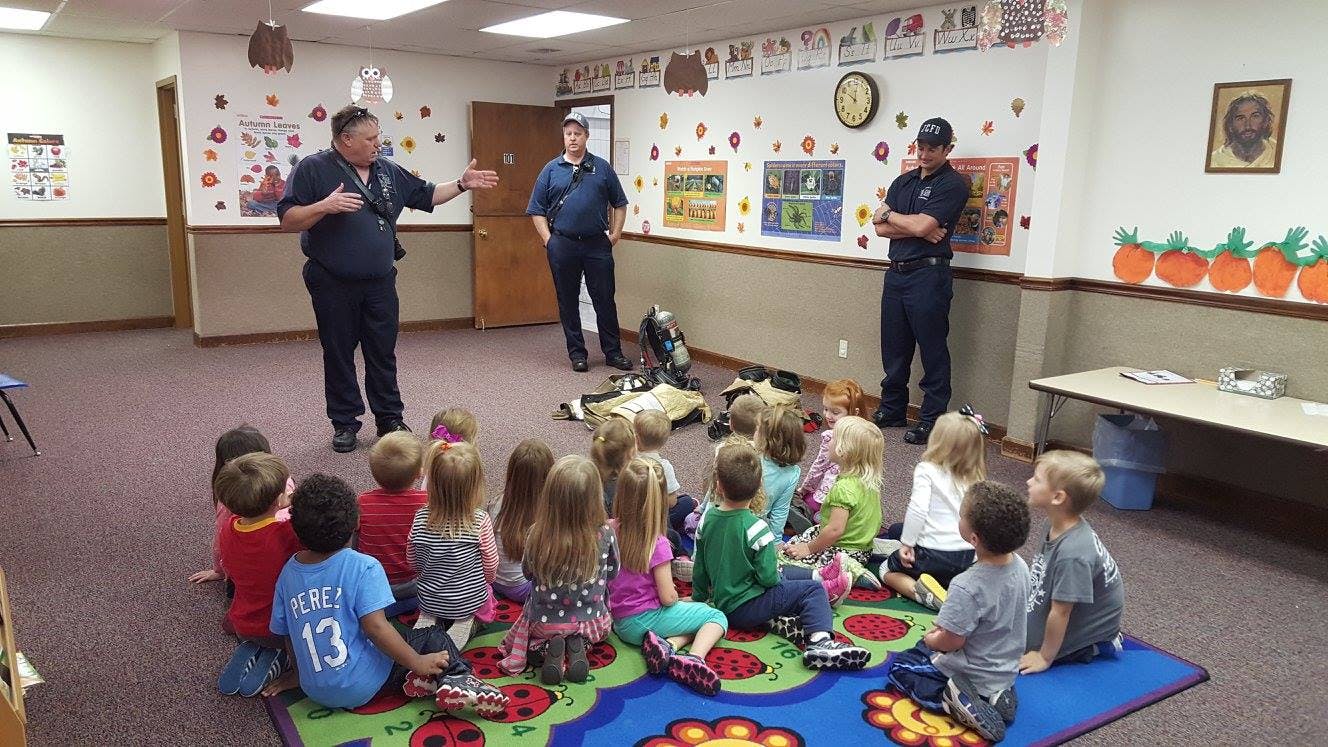 Three people in uniform speaking to a group of children sitting on a rug
