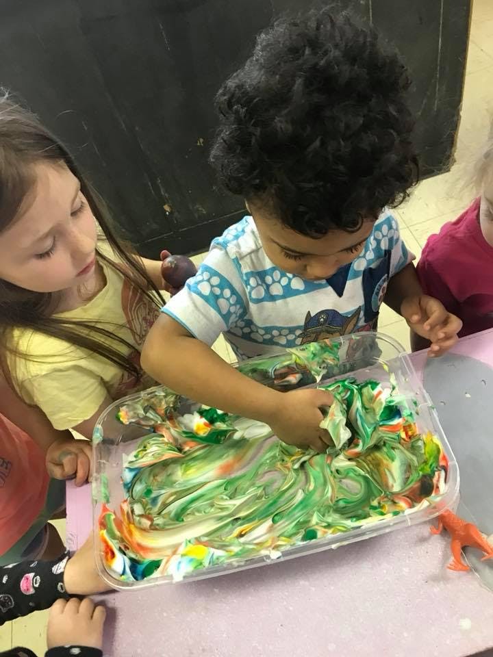Child playing with colorful shaving cream in a plastic bin