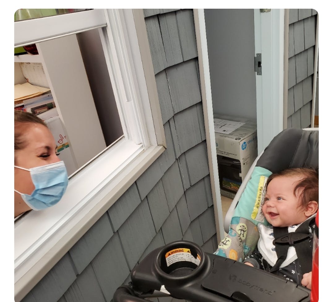Person in mask looking through window at child in stroller