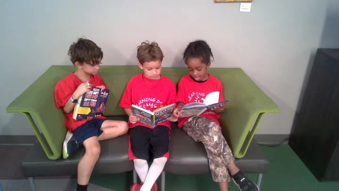 Three children sitting on a bench reading books