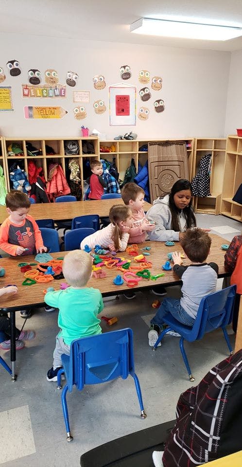 Children and an adult playing with colorful objects at a table in a classroom