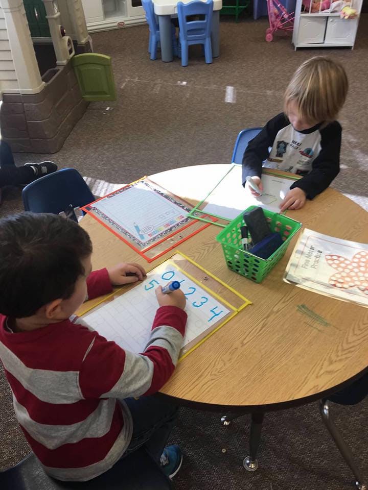 Two children writing on whiteboards at a round table