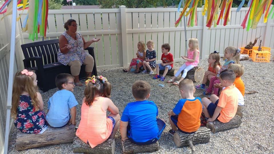 Adult person sitting on bench talking to children sitting on logs