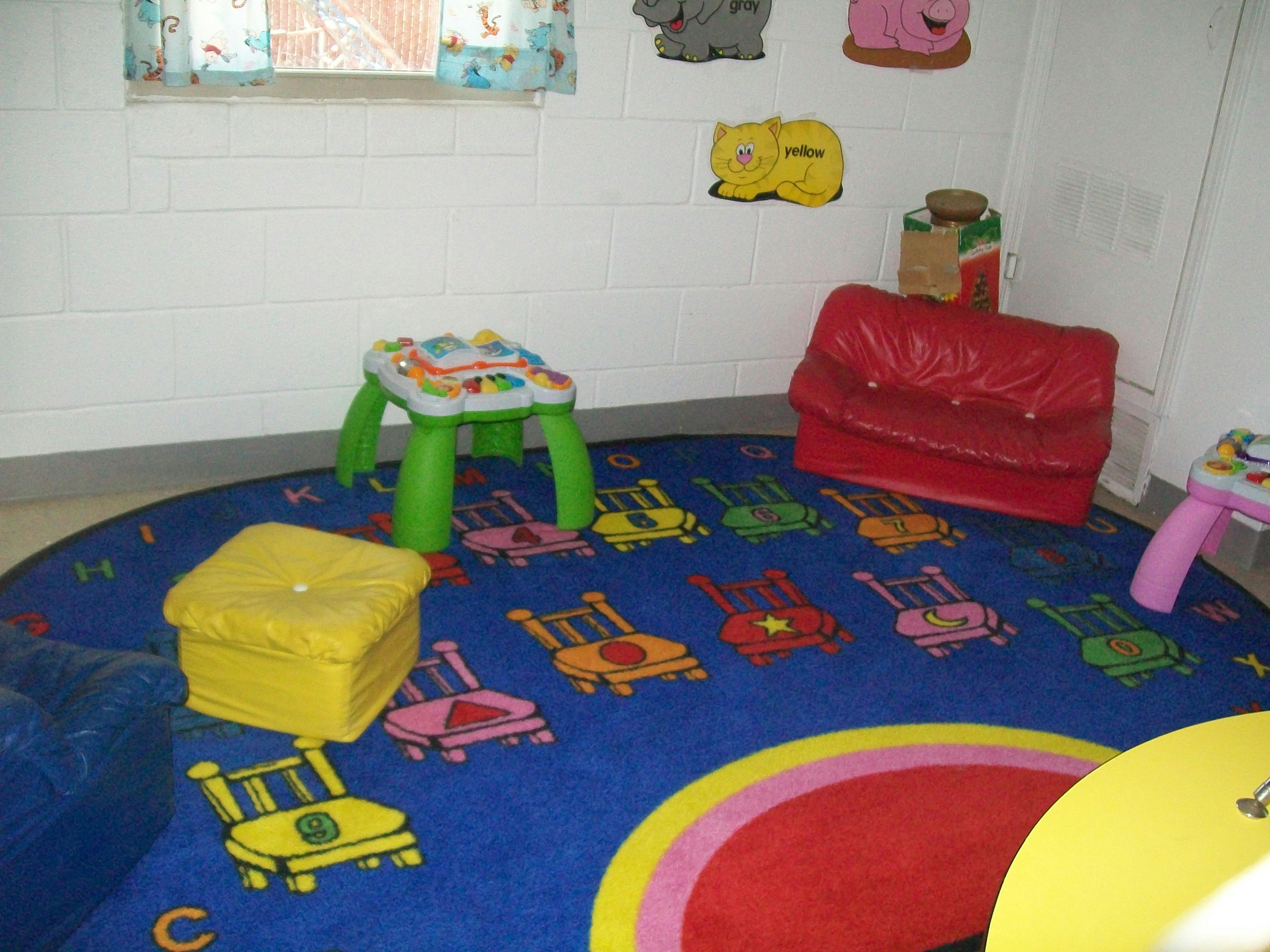 Playroom with a blue rug, small red couch, and toy tables