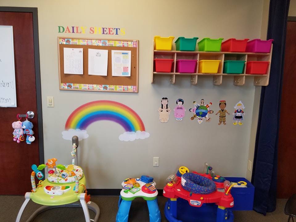 Childcare room with bulletin board, toy storage, rainbow decoration, and baby toys