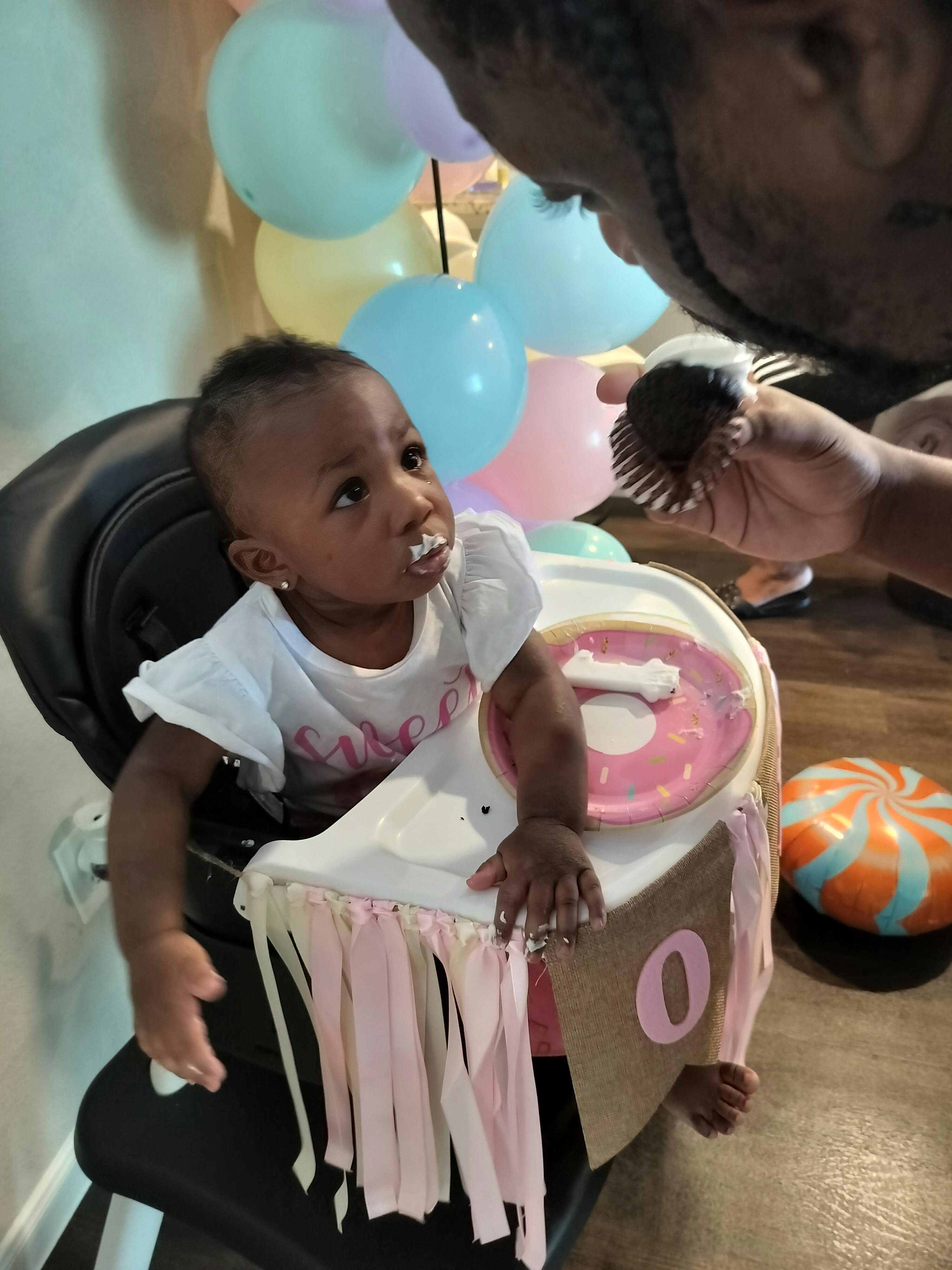 Child in high chair with frosting on face, person holding cupcake