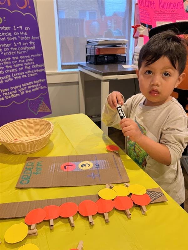 Child holding a marker at a table with craft supplies