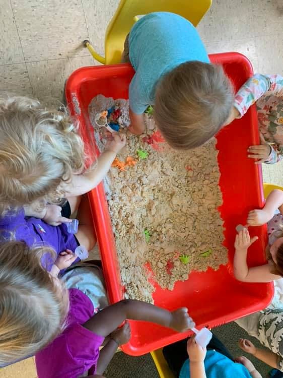 Children playing with sand in a red bin