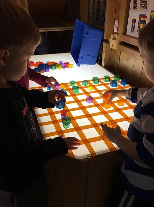 Two children playing with colorful translucent blocks on a light table