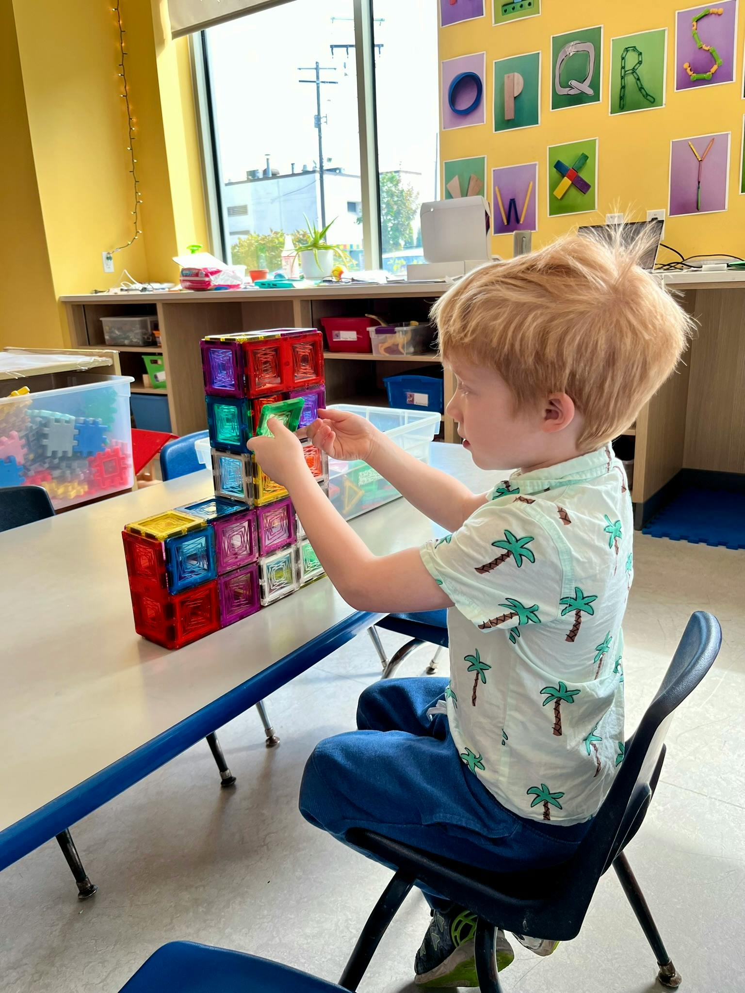 Child building with colorful magnetic blocks at a table in a classroom