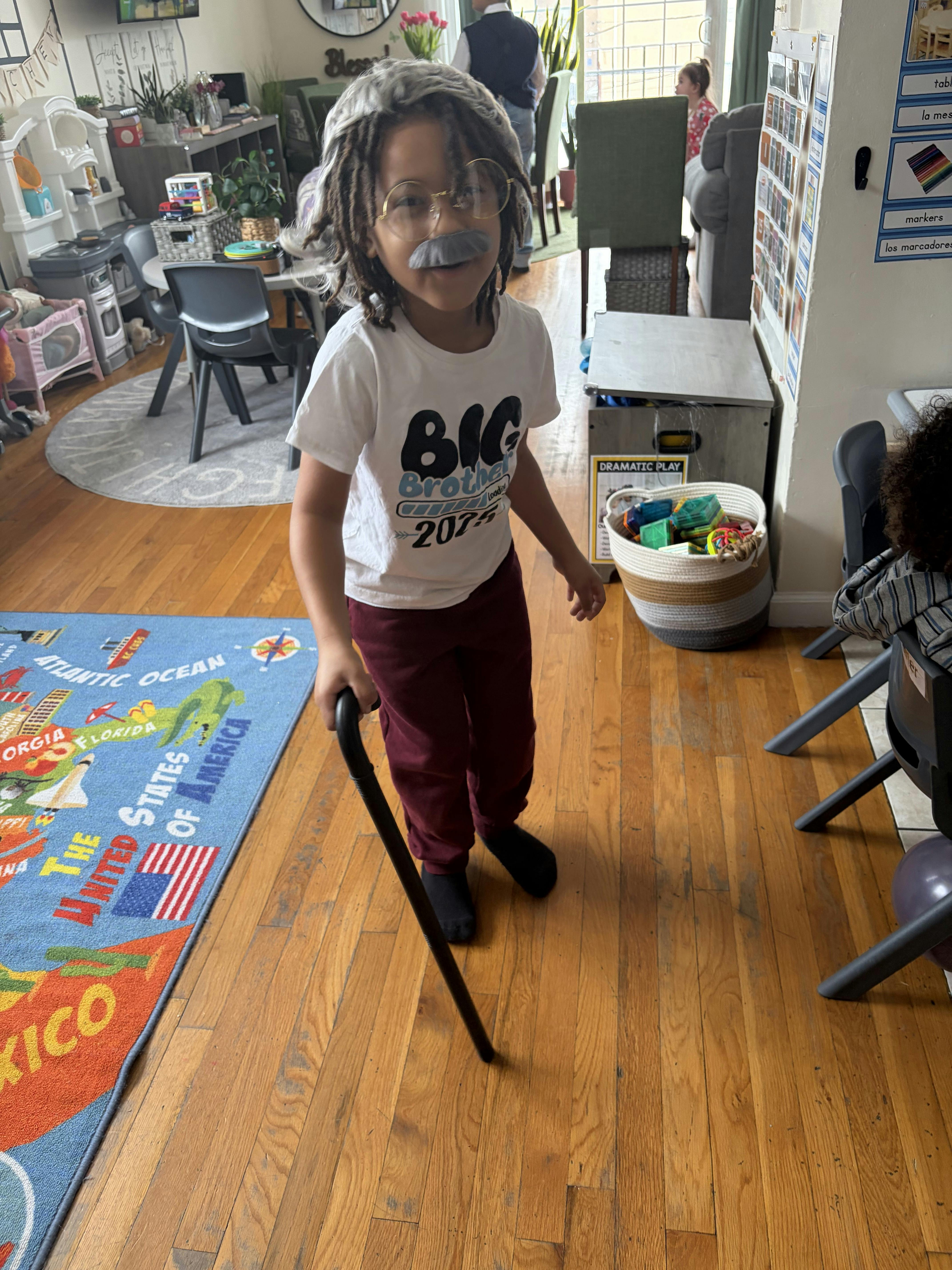 Child dressed as an elderly person with a wig, glasses, mustache, and cane