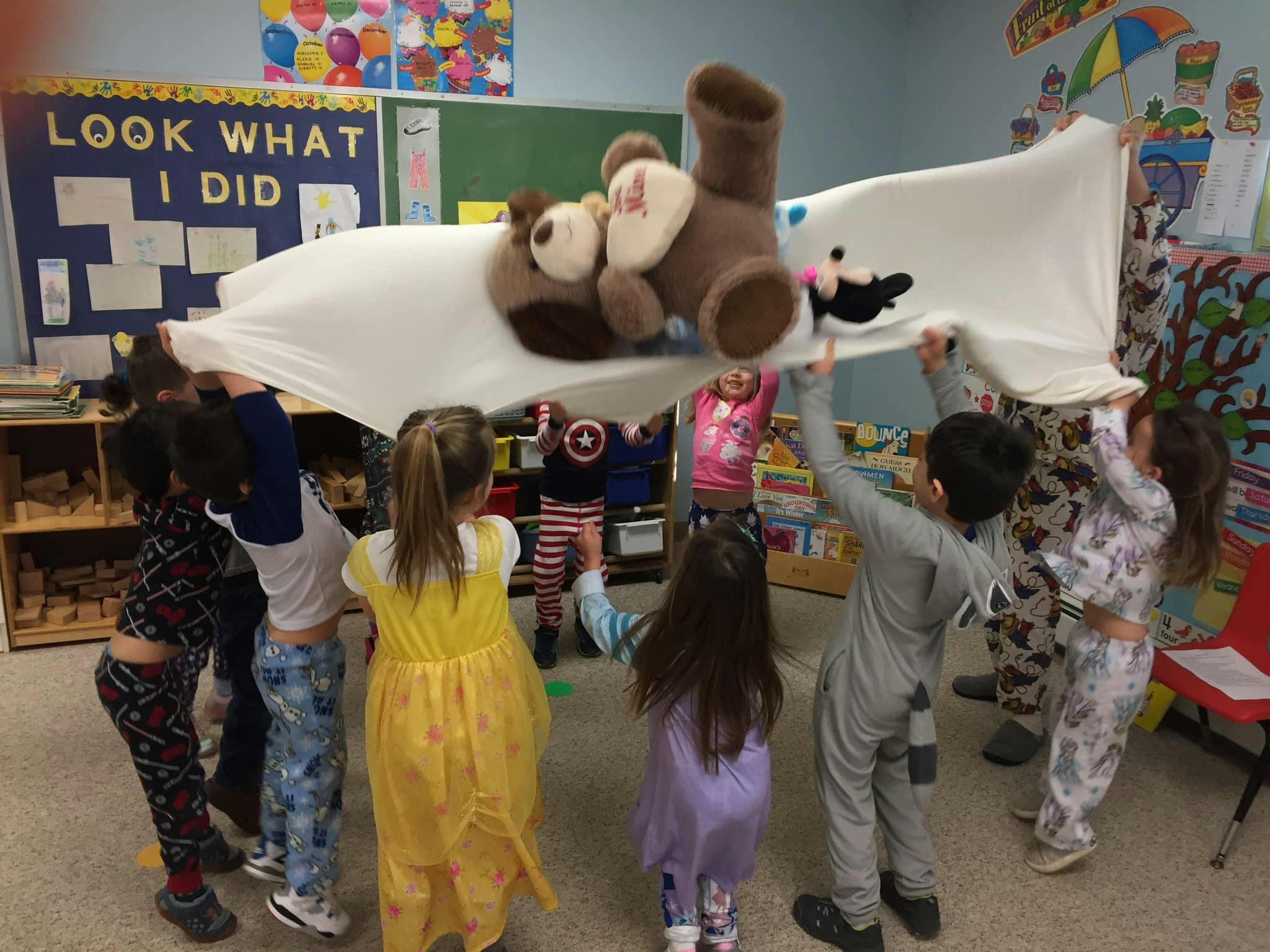 Children holding up a sheet with a teddy bear on top