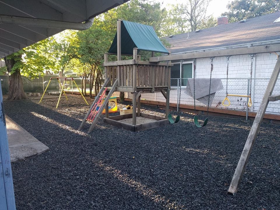 Outdoor playground with a wooden playset, slide, and swings