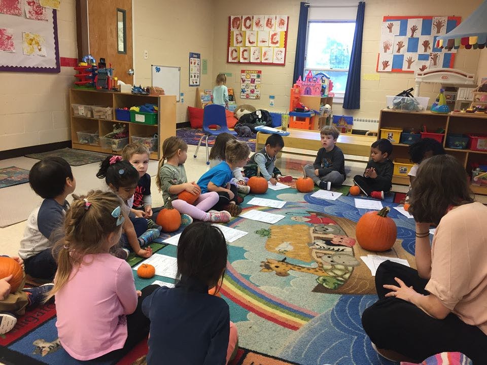 Children and adults sitting on a rug with pumpkins and papers