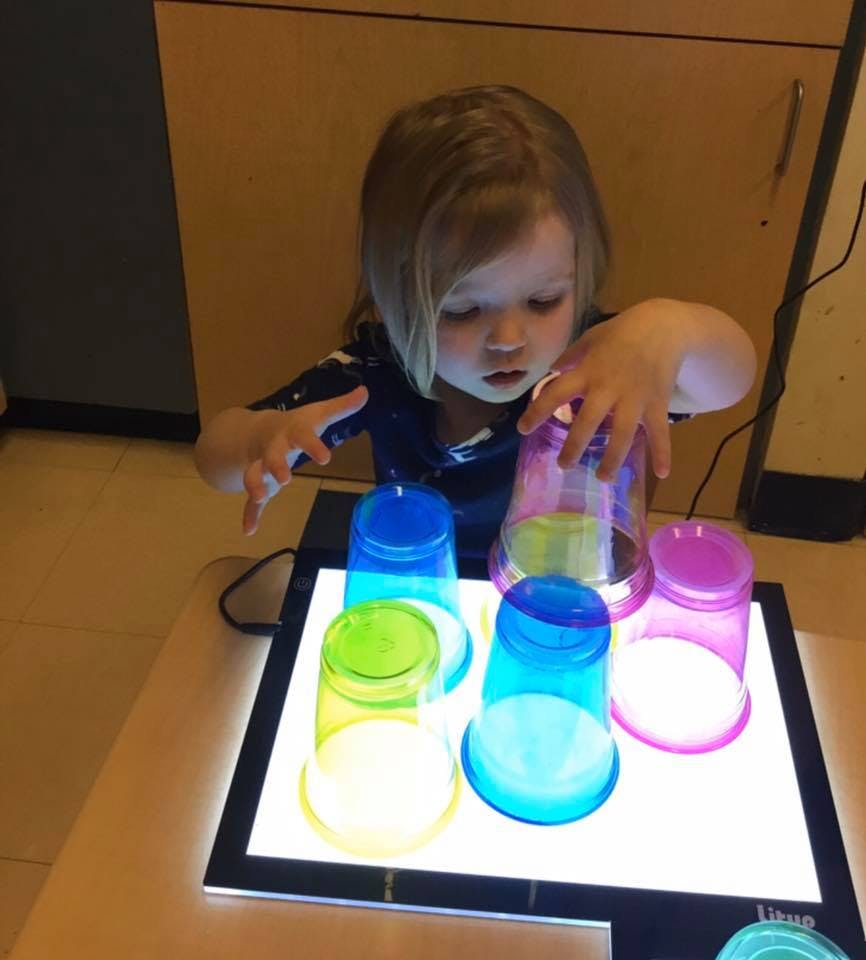 Child playing with colorful translucent cups on a light table