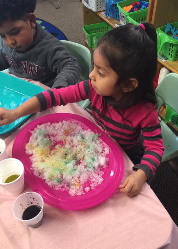 Child adding liquid to colorful snow on a pink plate