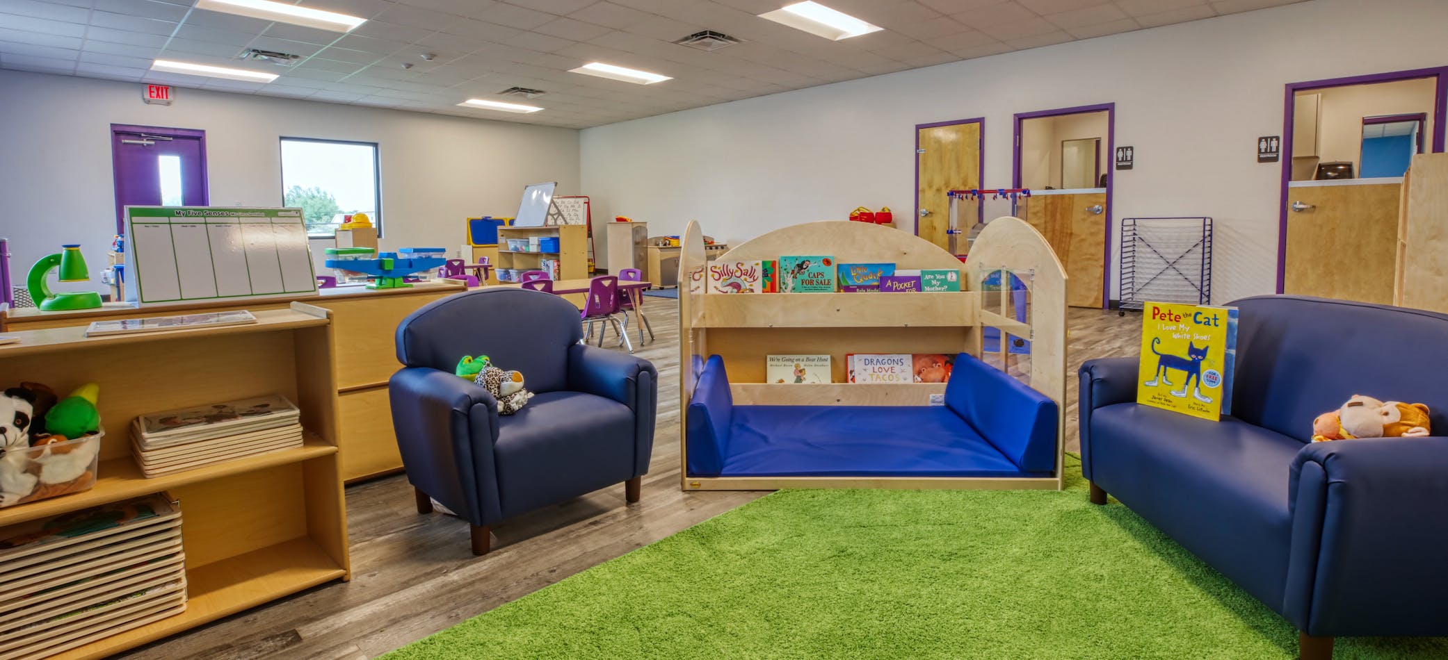Classroom with blue chairs, a green rug, and child-sized furniture with books