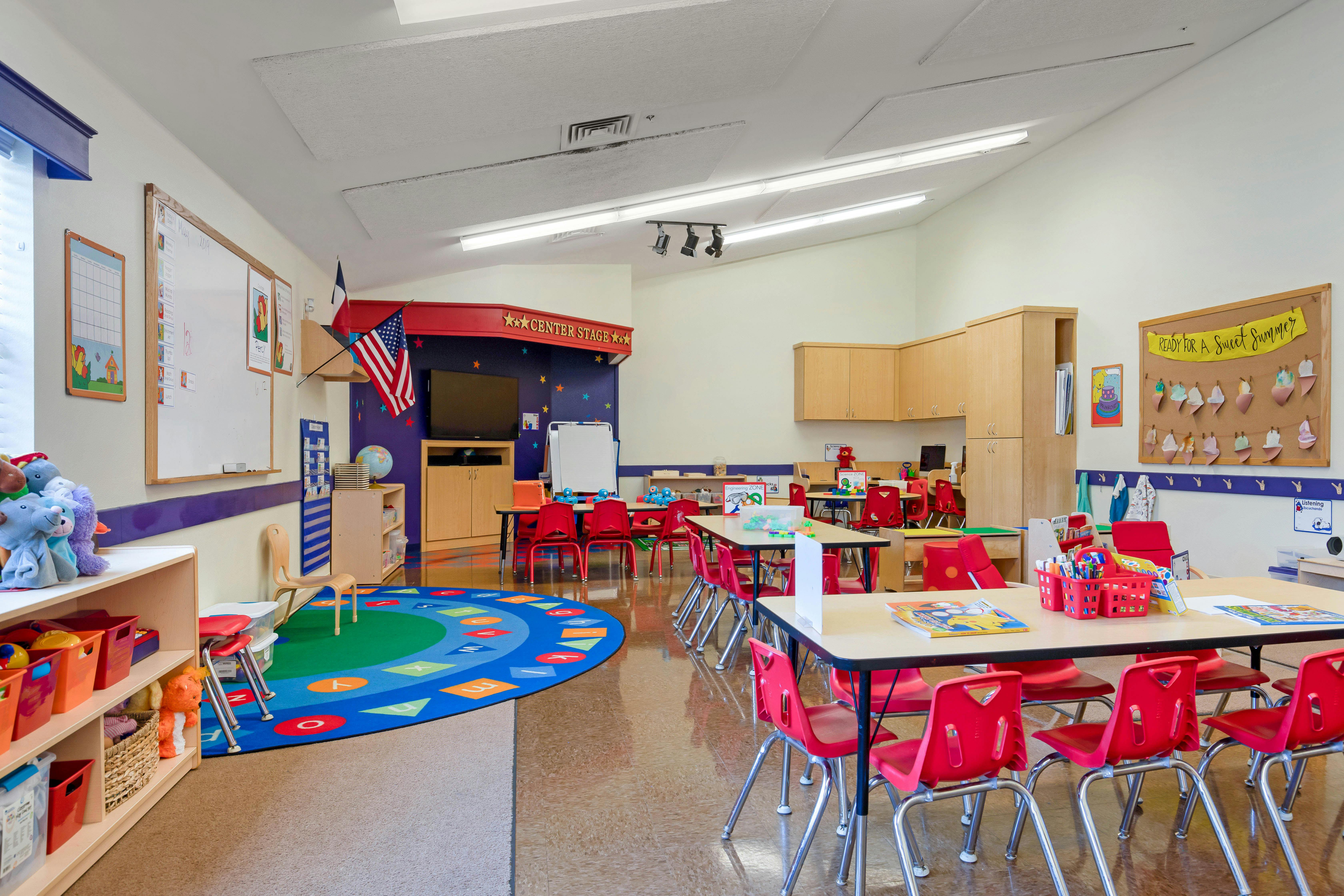 Empty classroom with small red chairs, tables, and a colorful alphabet rug