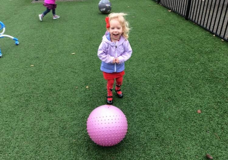 Child standing on artificial grass with a large pink ball
