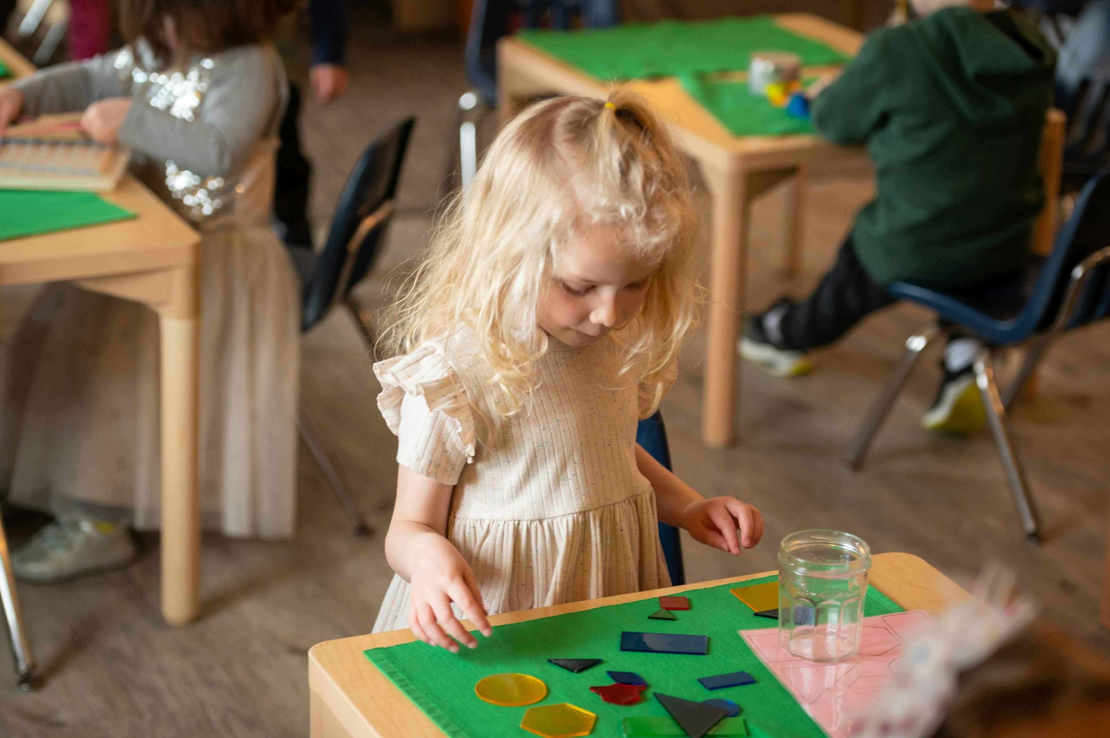 Child with blonde hair playing with colorful shapes at a table