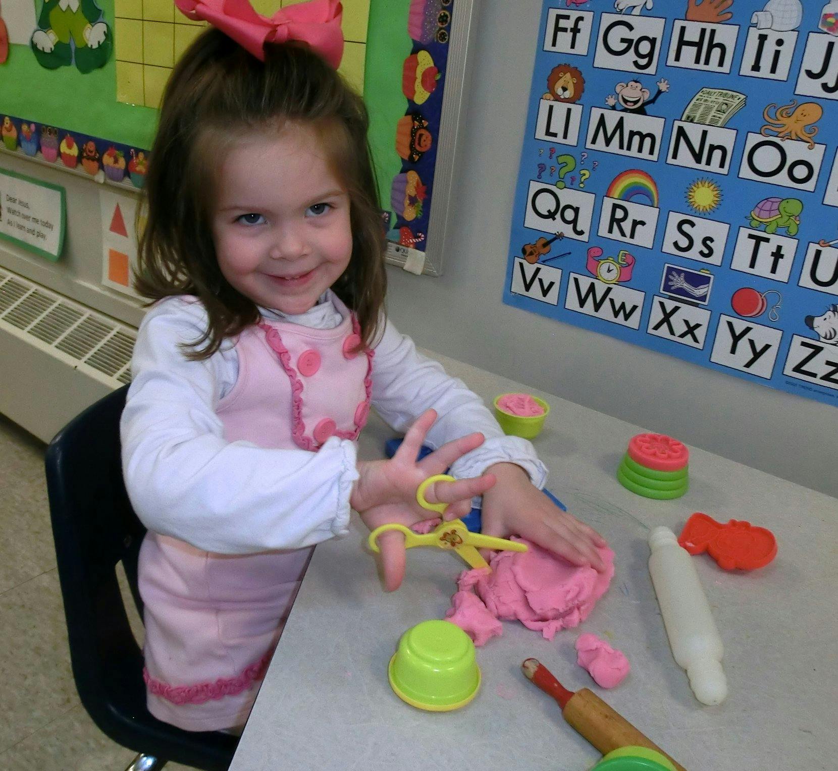 Child playing with modeling clay and toy scissors at a table