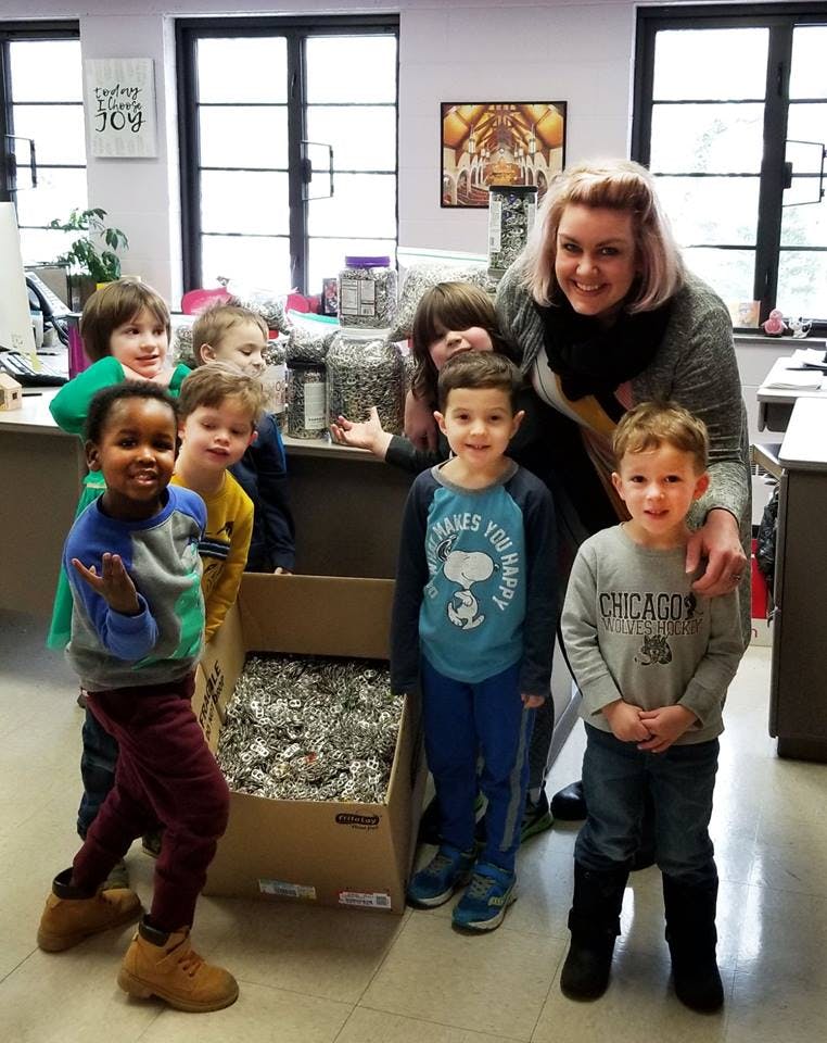 Adult and multiple children standing around a box of aluminum foil balls