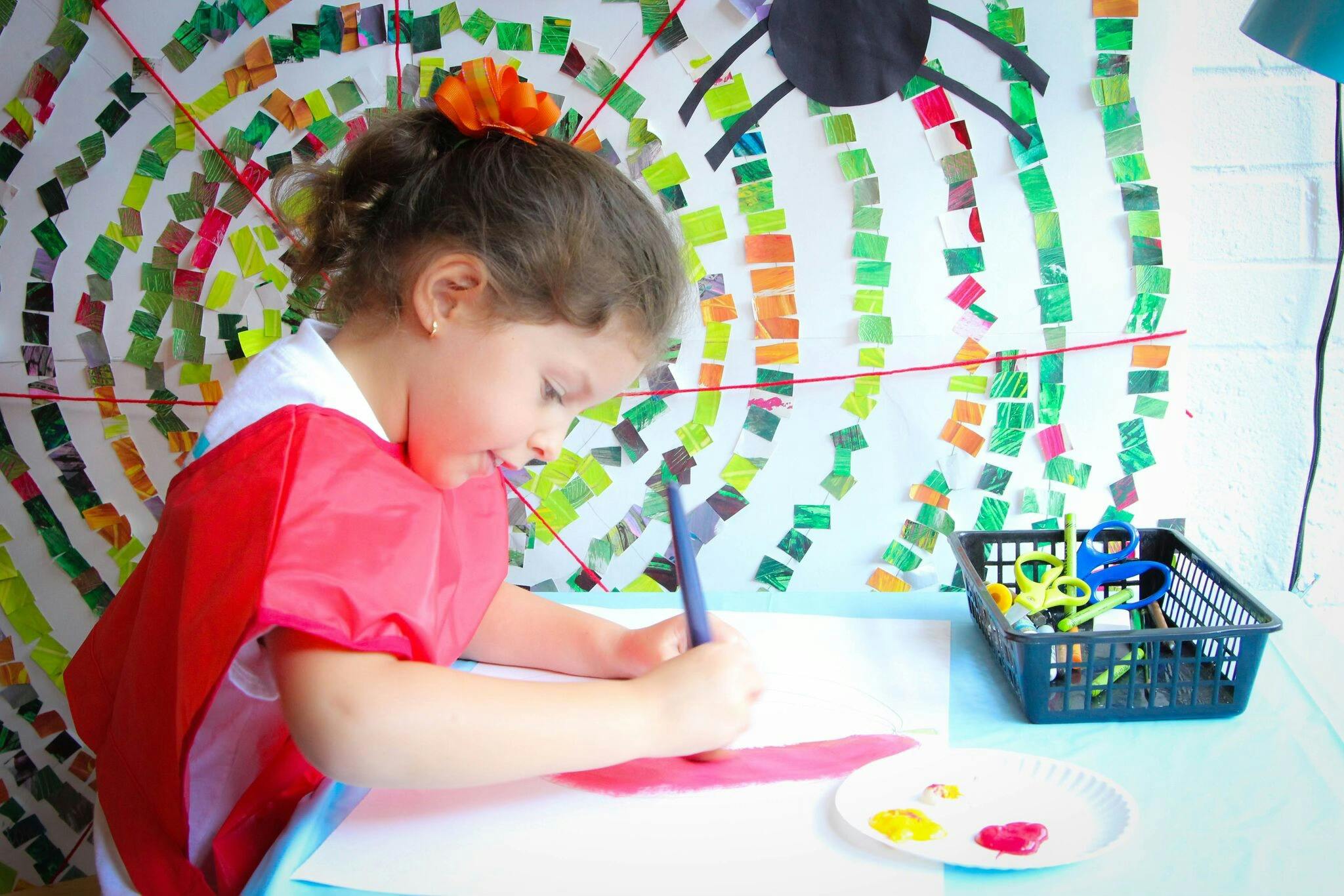 Child in a red smock drawing at a table