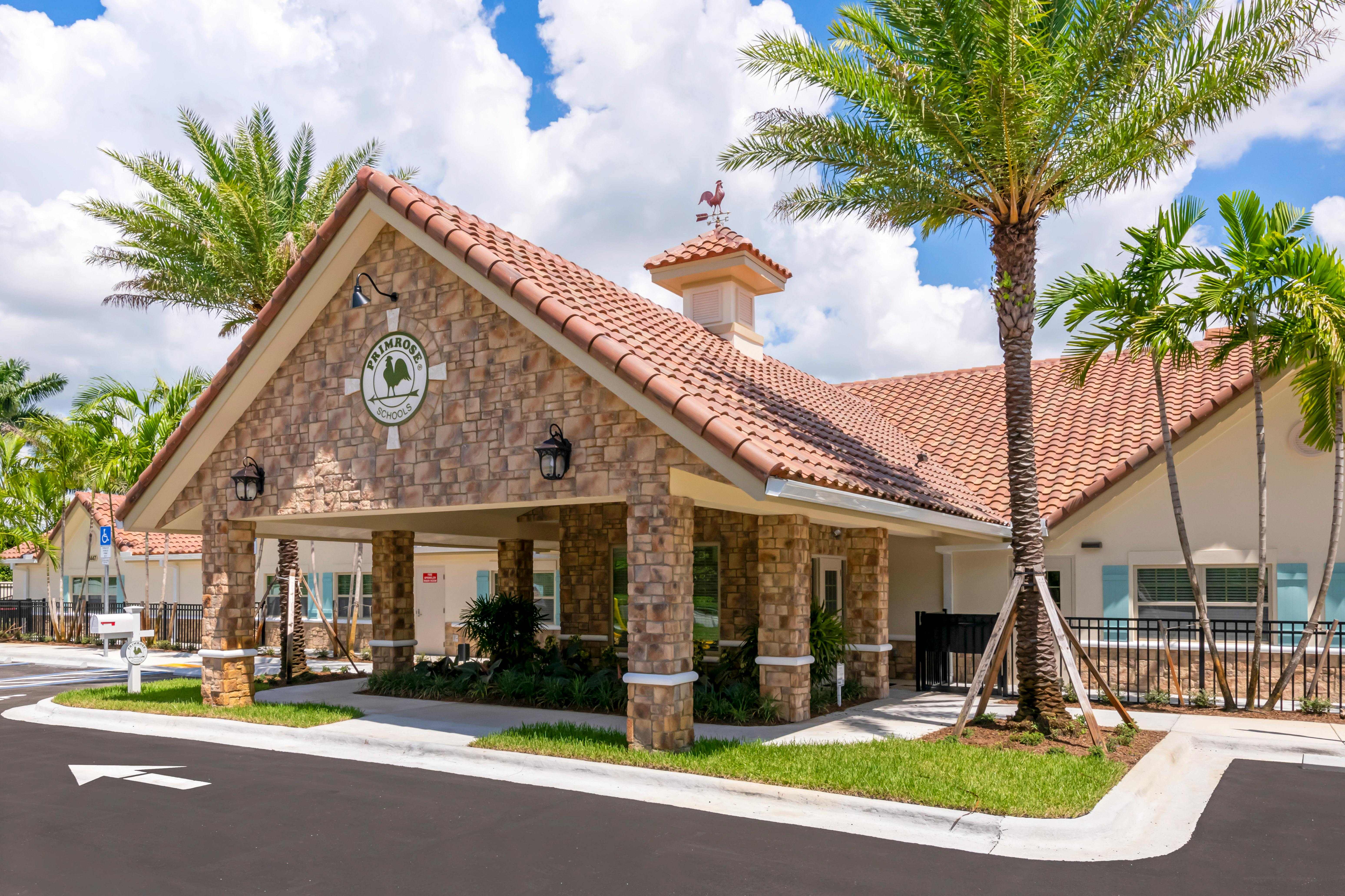 Entrance to a school building with a tile roof, stone facade, and palm trees