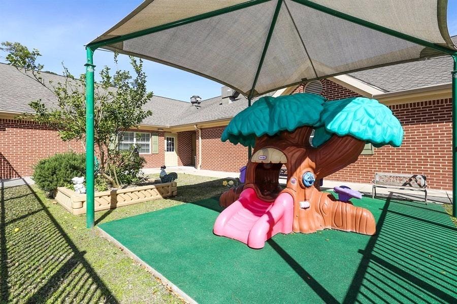 Playground with a tree-shaped play structure and a pink slide under a shade canopy