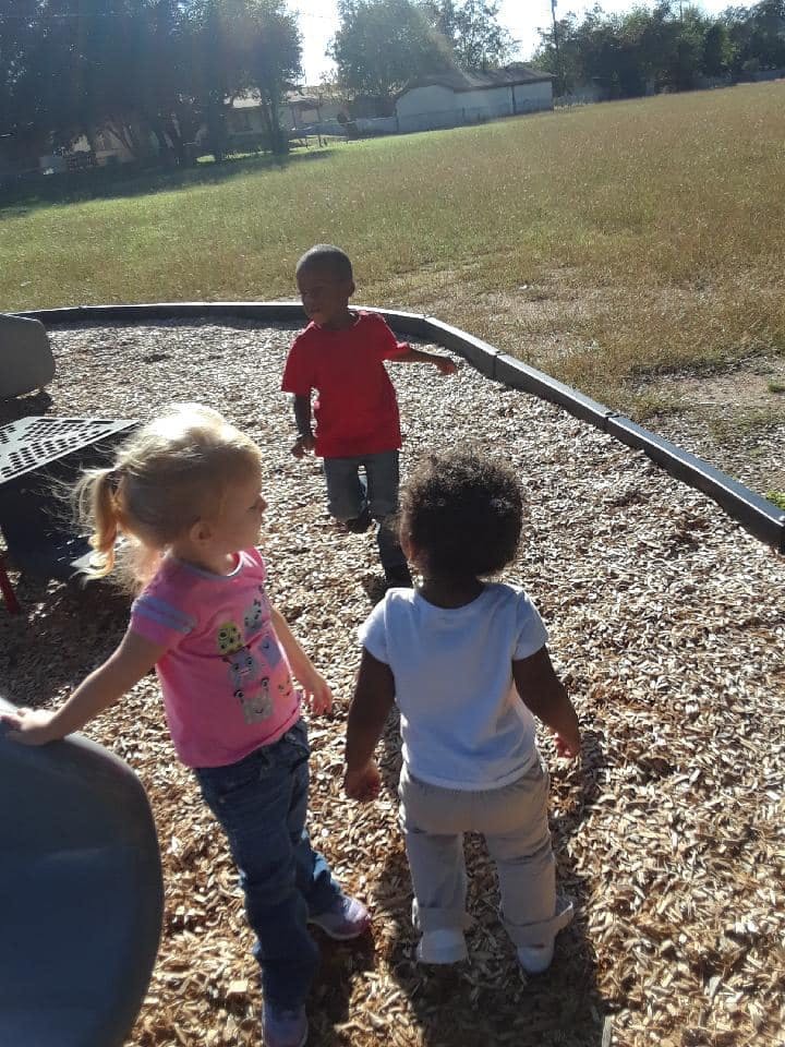 Three children on a playground with wood chips