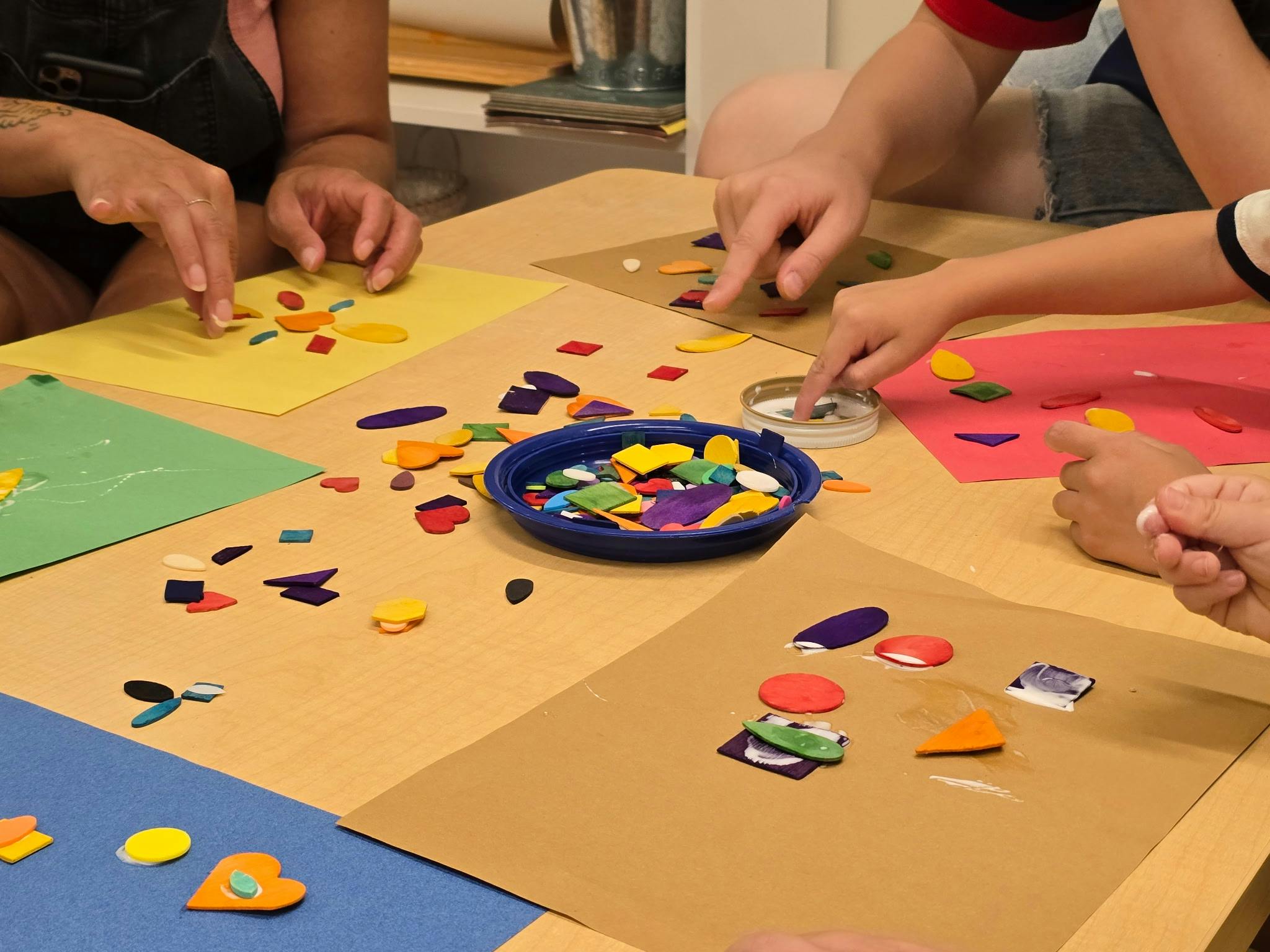 People arranging colorful foam shapes on paper at a table