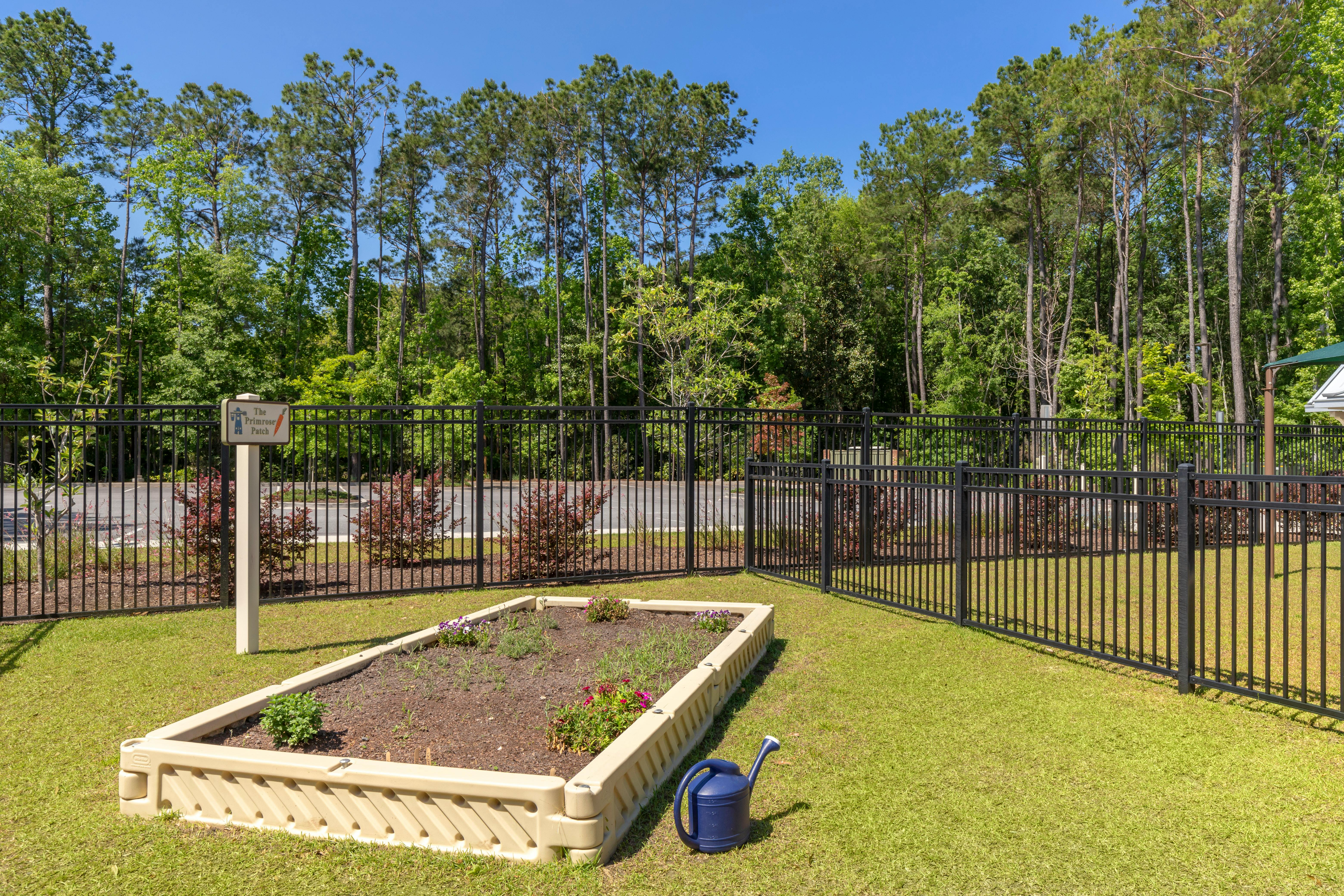 Raised garden bed next to a black fence with a sign, surrounded by green grass