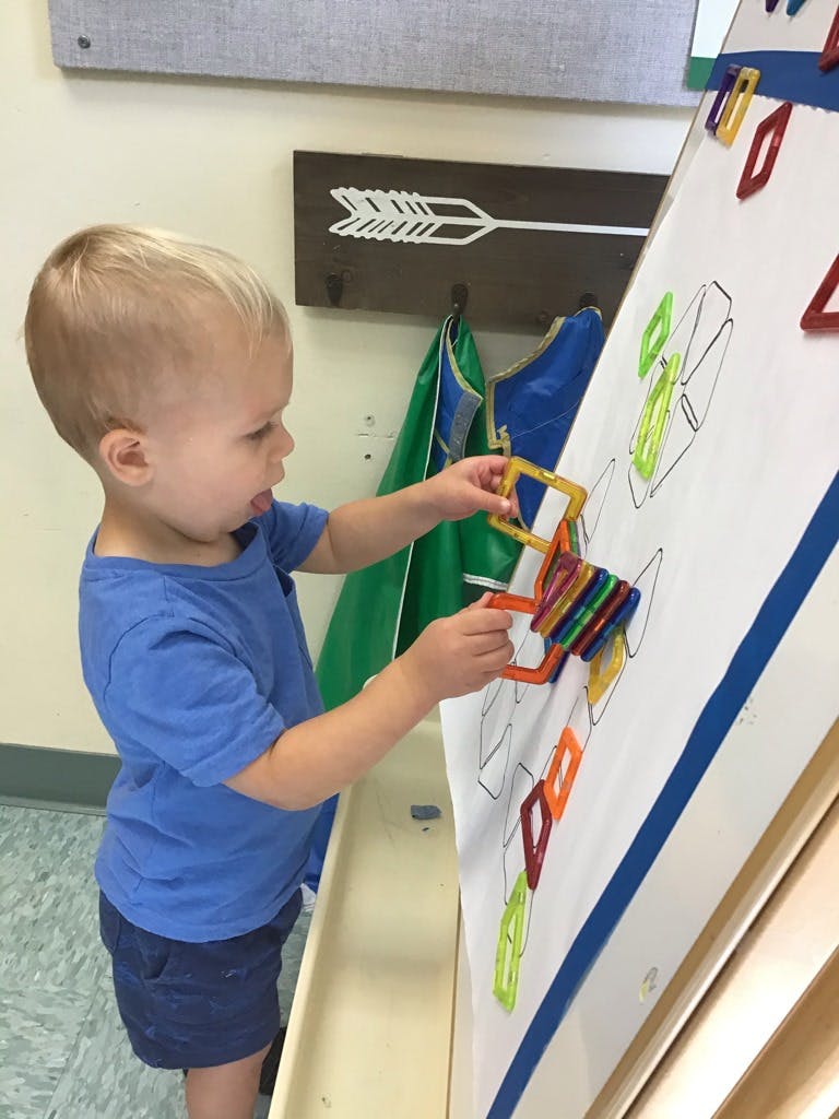 Child playing with colorful magnetic shapes on a white board