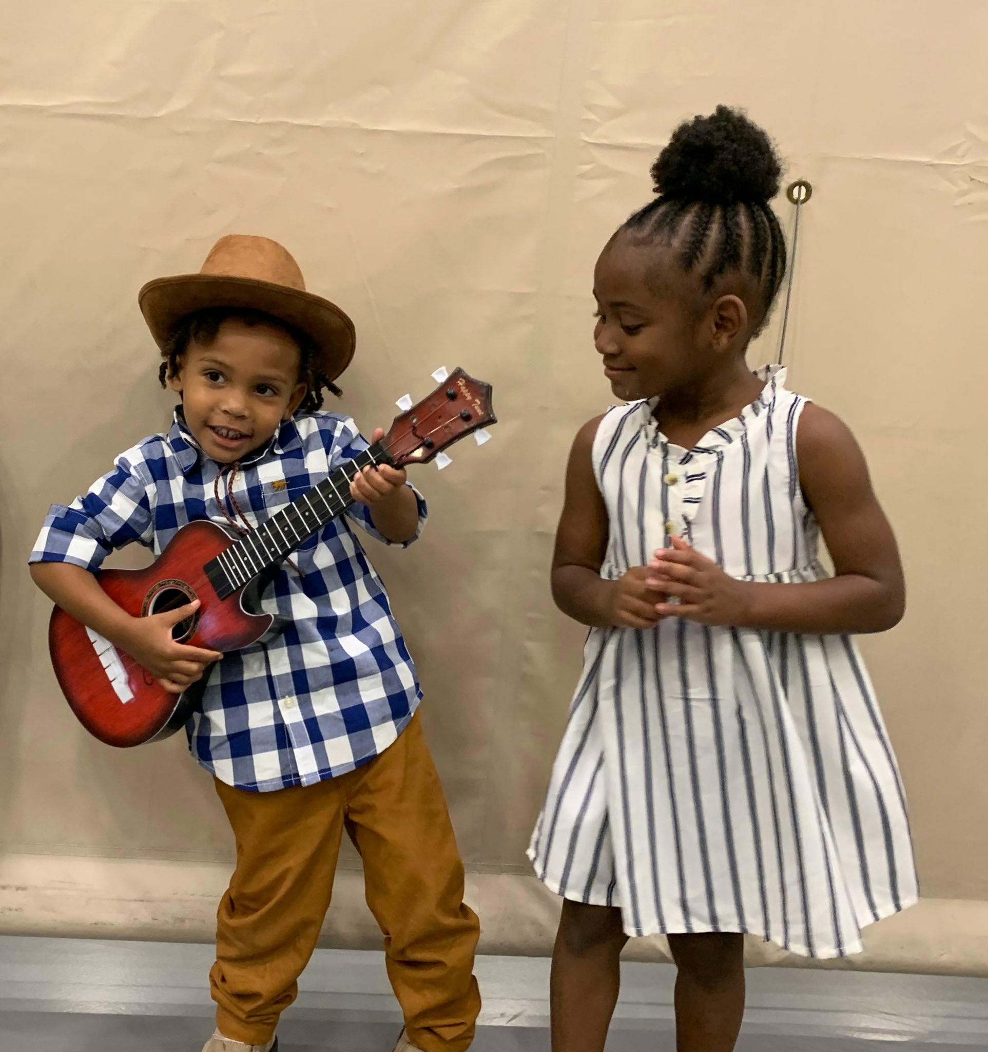 Child in hat playing guitar next to another child