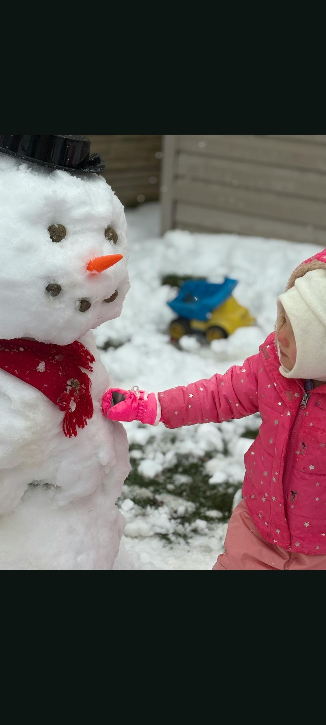 Child in winter clothing touching a snowman