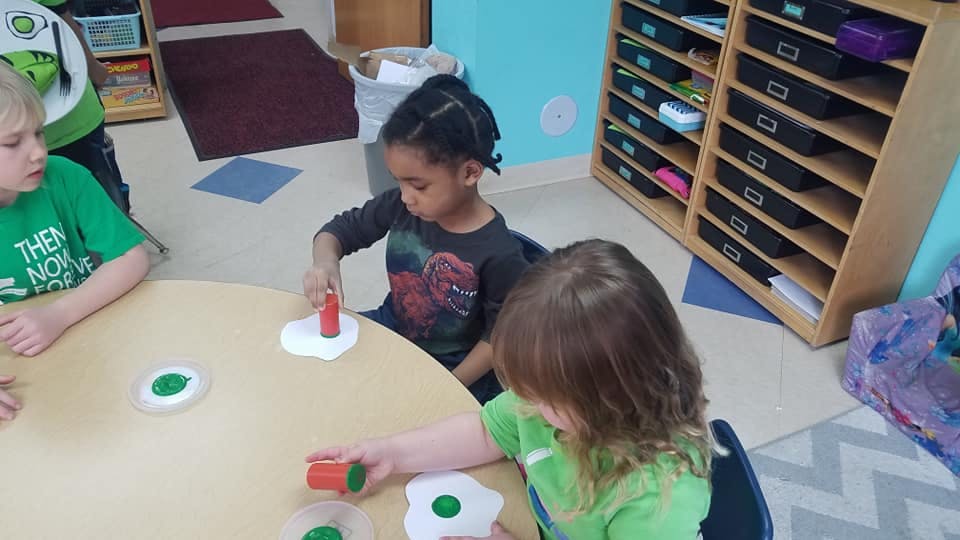 Three children playing with toys at a round table in a classroom