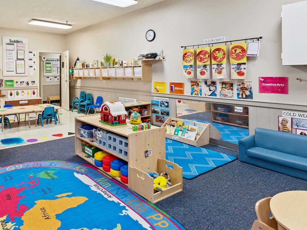 A colorful empty classroom with a world map rug and children's furniture