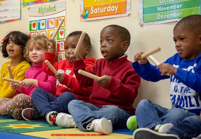 Children sitting on the floor playing with rhythm sticks in a classroom