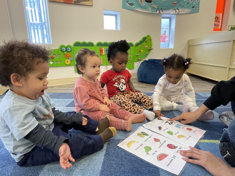 Four children sitting on the floor looking at a book with a person