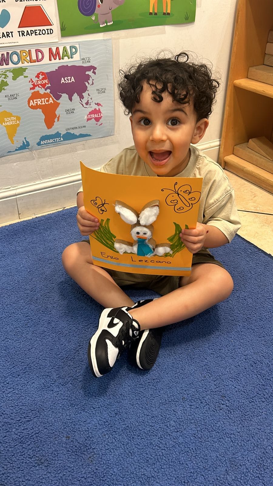 Child sitting on floor holding up a craft with a bunny
