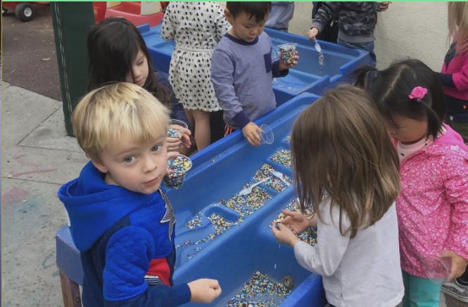 Children playing with water and small objects in blue bins