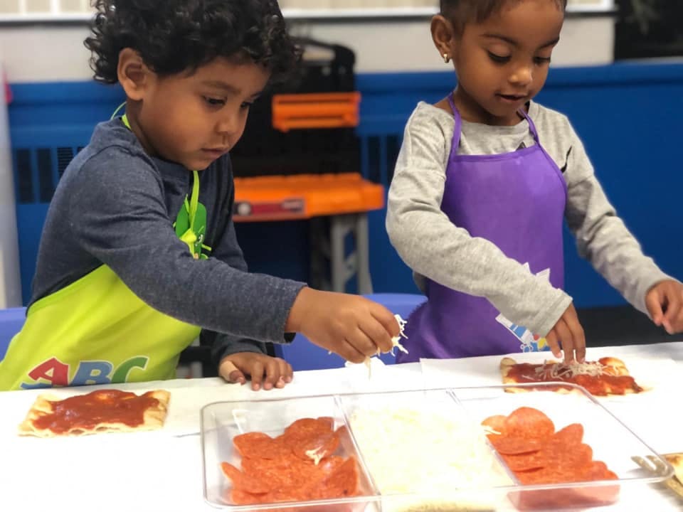 Two children in aprons making mini pizzas